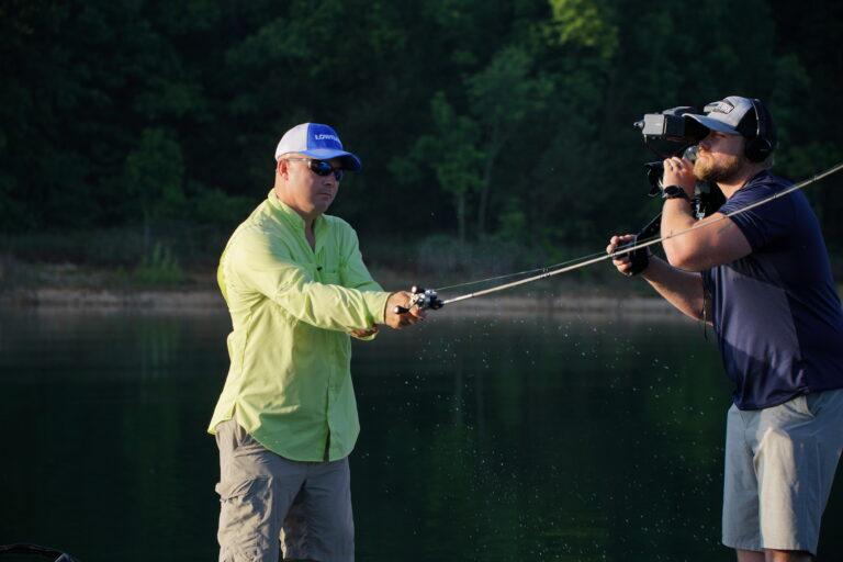 A cameraman on a boat taking video of an angler to create fishing guide advertising.