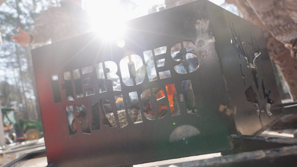 Beatiful shot of a firepit with sunrays shining through lettering that says Heroes Ranch. A screen shot from our Outdoor Media Production team.